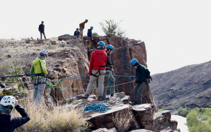 a group of outward bound students wearing rock climbing gear stand on cliffs and prepare to rappel down